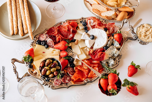 Food antipasto prosciutto ham, salami, olives and grissini bread sticks. cheese on a board parmesan, pecorino, gorgonzola. Charcuterie board. Two glasses of red wine 
