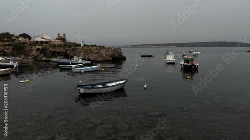 A fishing port with boats moored against a rocky coast on a cloudy day
