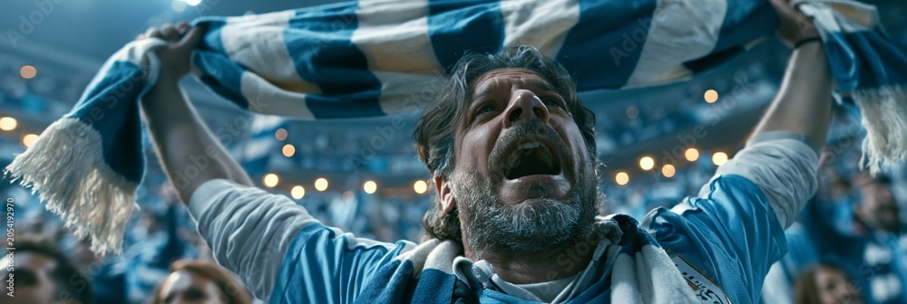 Naklejka premium Passionate Uruguay football fan raises a national scarf above head wearing the team jersey captured from a dynamic lowangle perspective at a lively stadium.