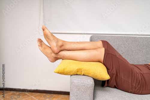 Woman relaxing on sofa elevating tired legs at home