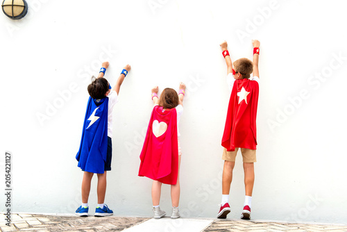Fotografija Three kids in superhero capes facing a wall, pretending to fly.