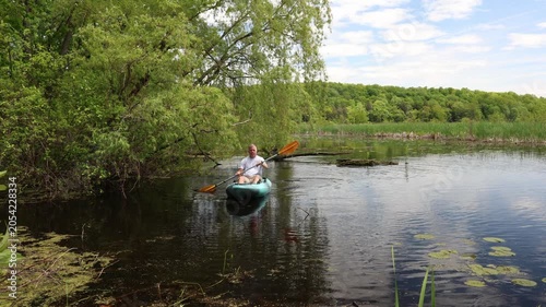 Middle-aged kayaker paddling and approaching the river shoreline