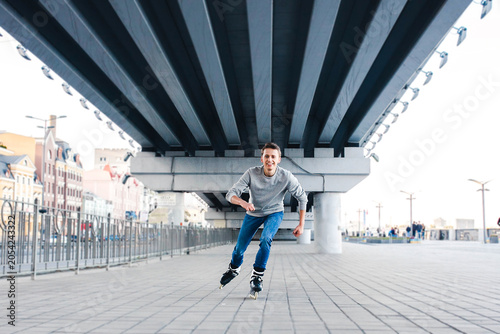 Φωτογραφία Smiling man rollerblading on urban promenade under bridge