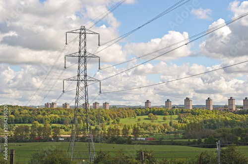 Electricity Pylon Above Forest and High Rise Apartment Blocks on Sunny Day  with White Clouds
