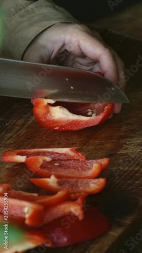 Vertical video. Cooking summer vegetables. Slicing sweet red bell pepper on cutting board