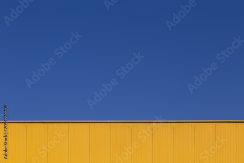 Abstract industrial background with blue sky and yellow warehouse wall