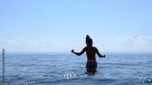 Happy girl is having fun and dancing on the beach, fully enjoying life. Carefree girl, dressed in a summer bathing suit, breathes in the fresh sea air, cheerfully smiling.  Pure joy  moment.