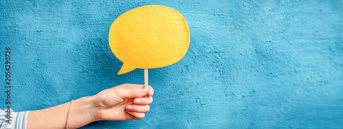 Hand holding a yellow speech bubble in front of a blue wall during a creative project at an indoor location