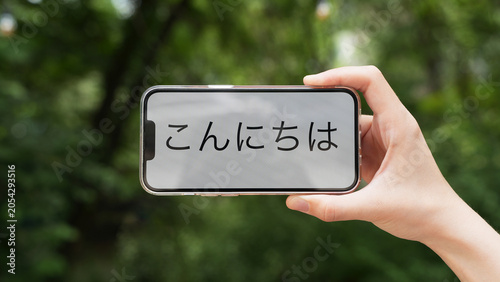 Hand holding a smartphone with a message 'Konichiwa' (hello) in Japanese, blurred background