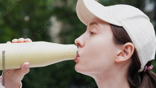 extreme close up of a young woman drinking water from reusable yellow thermos bottle, hydration, sustainable living, modern lifestyle