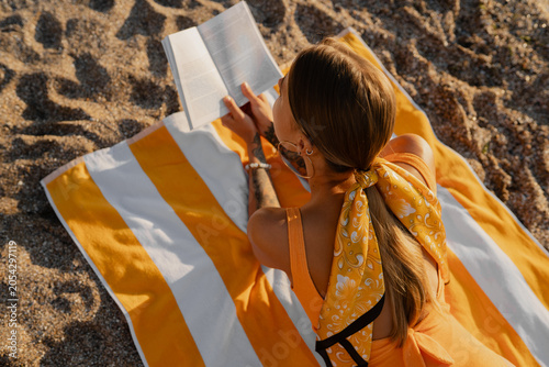 Картината върху платно beautiful blond woman lying on beach reading book on summer season vacation wear