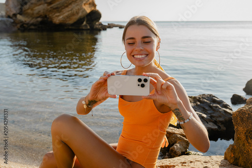 Fotografie attractive young smiling blonde happy woman in yellow swimsuit sitting on beach