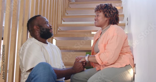 African American couple holding hands, laughing after tease, showing love, leaning on home stairs