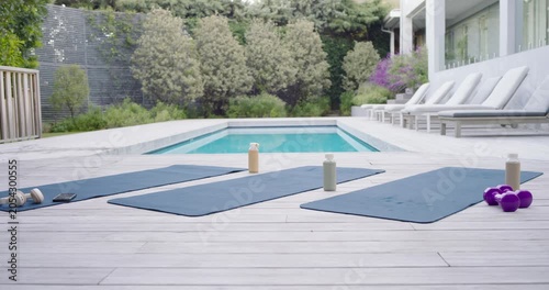 Camera is sliding left, three blue yoga mats are holding bottles on wooden deck for workout