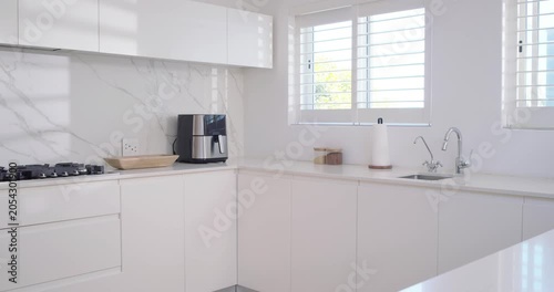 Sun sliding past slats, casting bands across counter, airfryer, camera panning right revealing sink