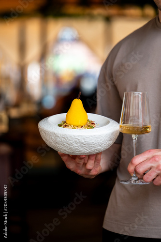 Quadro em tela A person holding a textured white bowl with a pear-shaped dessert and a glass of white wine