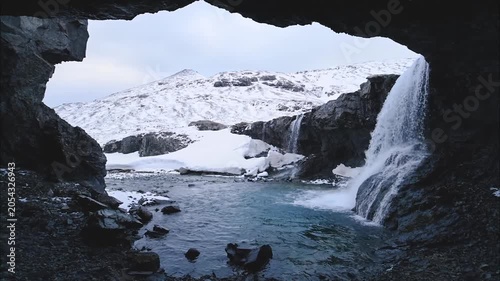 Cinematic Shot of Waterfall Inside Volcanic Cave withSnow Mountain