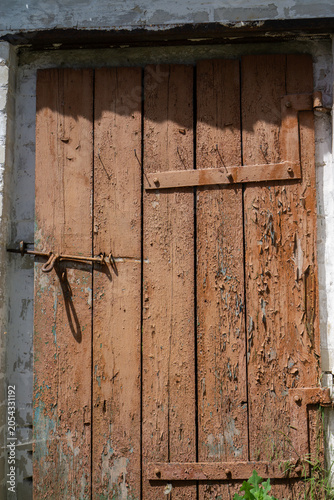 Old brown wooden door with a rusty metal latch and hinges on a white wall.