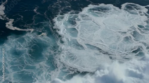 Top-down view of ocean waves creating abstract sea foam patterns on deep blue water. Ideal for nature, marine, travel, environment, and background concepts.