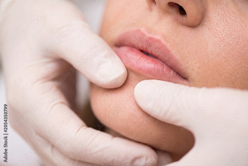 Naklejka premium Close-up of a person's lips and chin being gently examined by gloved hands, cosmetic procedure concept.