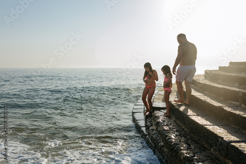 Slika na platnu Backlit Father and two daughters Walking Along Seaside Steps at Sunset