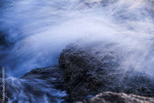 Artistic Long Exposure Photography of Rushing Ocean Waves Crashing Over Rugged Dark Coastal Rocks at Twilight