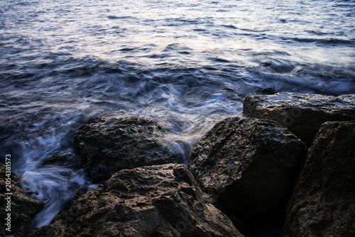 Artistic Long Exposure Photography of Rushing Ocean Waves Crashing Over Rugged Dark Coastal Rocks at Twilight