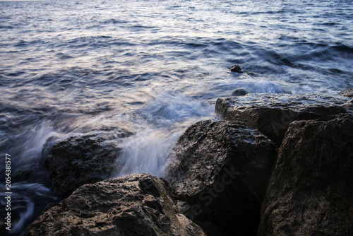 Artistic Long Exposure Photography of Rushing Ocean Waves Crashing Over Rugged Dark Coastal Rocks at Twilight