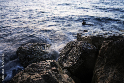 Artistic Long Exposure Photography of Rushing Ocean Waves Crashing Over Rugged Dark Coastal Rocks at Twilight