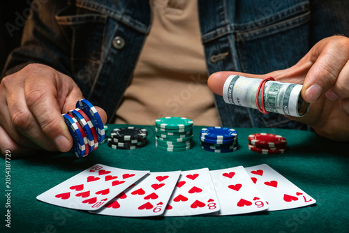 фотографія Two hands hold poker chips and cash while several playing cards lay face up on a green table