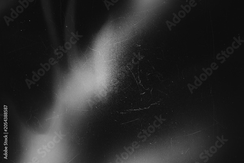 Dark grunge film dust and scratch texture overlay with soft light bloom on black background