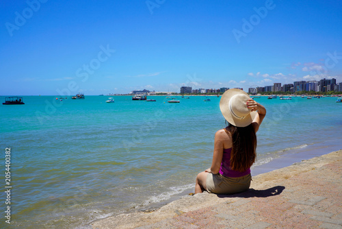 Holidays in Maceio, Brazil. Young woman sitting enjoying view towards natural swimming pools of Pajucara, Maceio, Brazil.