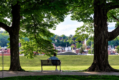 Foto Man sitting on a park bench framed by mature shade trees overlooking historic do