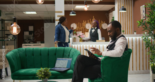 Quadro su tela African American staff making online bookings on tablet in lobby, working at luxurious hotel and providing excellent concierge service for guests upon their arrival, bellboy in uniform manage rooms