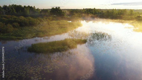 Flying over peaceful river and green fields during golden sunrise