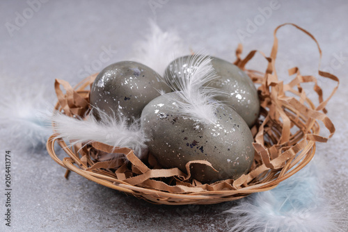 Fotografía Easter eggs in wicker nest with feathers rustic background