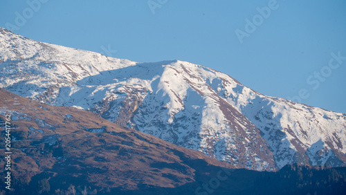 Snow covered mountain peak rising under clear blue sky with rocky slope