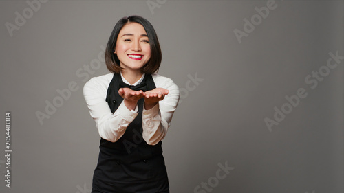 Foto Cute flirty waitress blowing air kisses in front of camera, acting romantic with sweet gesture, asian restaurant employee posing with a kissy facial expression, catering industry