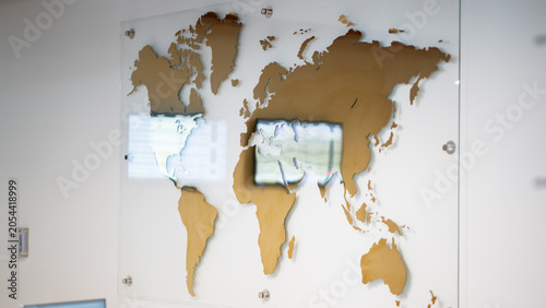 Golden world map wall art on glass panel mounted in modern office interior wall