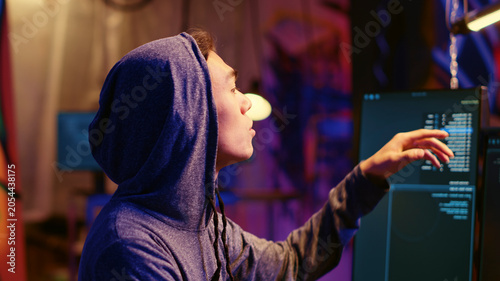Schilderij op canvas Hooded hacker talking with colleague while coding malware designed to exploit network backdoors, bypassing security measures such as logins and password protections, close-up shot