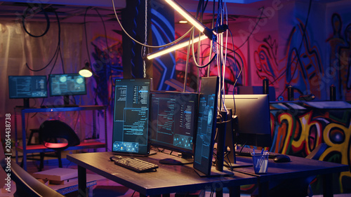 Canvas-taulu Panning shot of high tech computer system running malicious code in empty basement, PC monitors in empty neon lit criminal hideout used by hackers to commit illegal activities