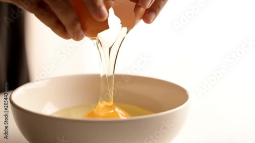 A person carefully cracks an egg into a white bowl in a kitchen for cooking in this close-up video