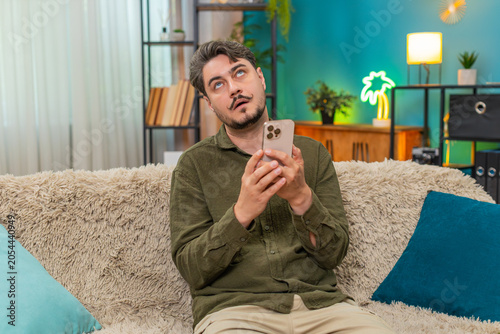 Foto Middle-aged man at home reads smartphone message rolls eyes sighs showing irritation frustration over bad news