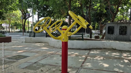Yellow and red outdoor shoulder rotation fitness equipment in sunny public park