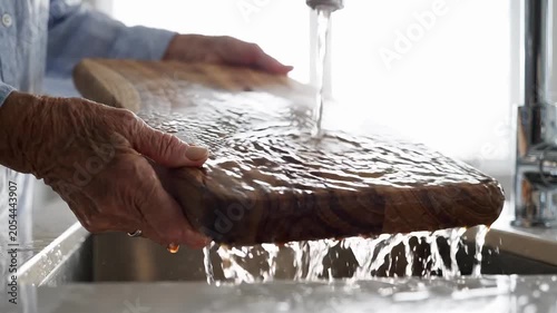 A person washing a cutting board under running water in a kitchen sink in a video about kitchen hygiene.