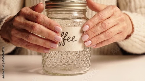 A person holds a glass jar labeled coffee on a table in a cozy setting in this video.