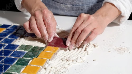 A person laying colorful mosaic tiles on a white surface in a creative video project