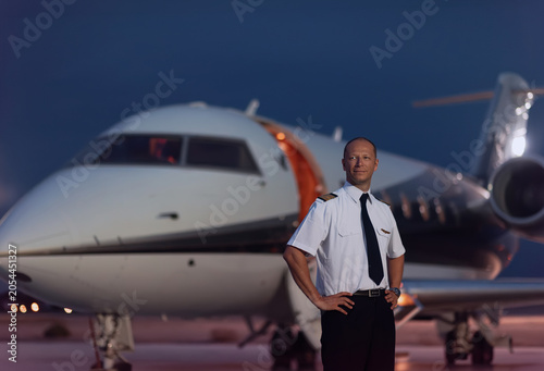 фотографія Confident male airline pilot in uniform standing with hands on hips on airport t