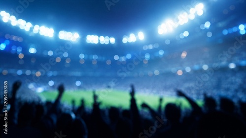 Large crowd of people cheers with raised hands in a brightly lit sports stadium during a night event.