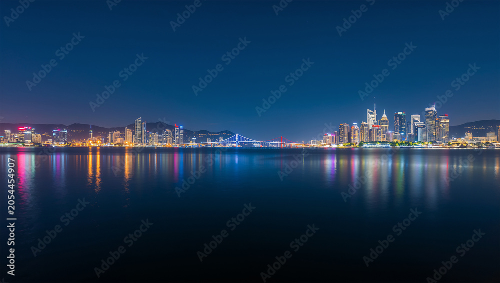 Fototapeta premium 夜の都市湾で高層ビルの光が水面に映るパノラマ風景